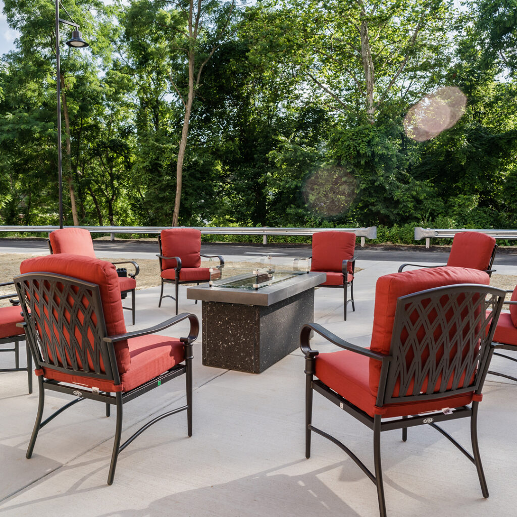 1-3-03-Residence-at-Whitehall-homepage-gallery - The Residence at Whitehall Red-cushioned chairs placed in a circle around a table outdoors, in front of many trees at The Residence at Whitehall, a great option for senior living in Allegheny County.