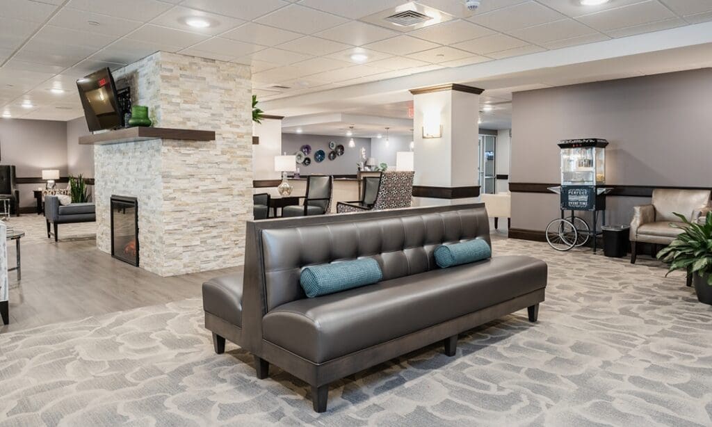 A lobby area with a long black couch, a popcorn machine, a TV, and tables with sofa chairs at The Residence at Whitehall, a great option for senior living in Allegheny County.