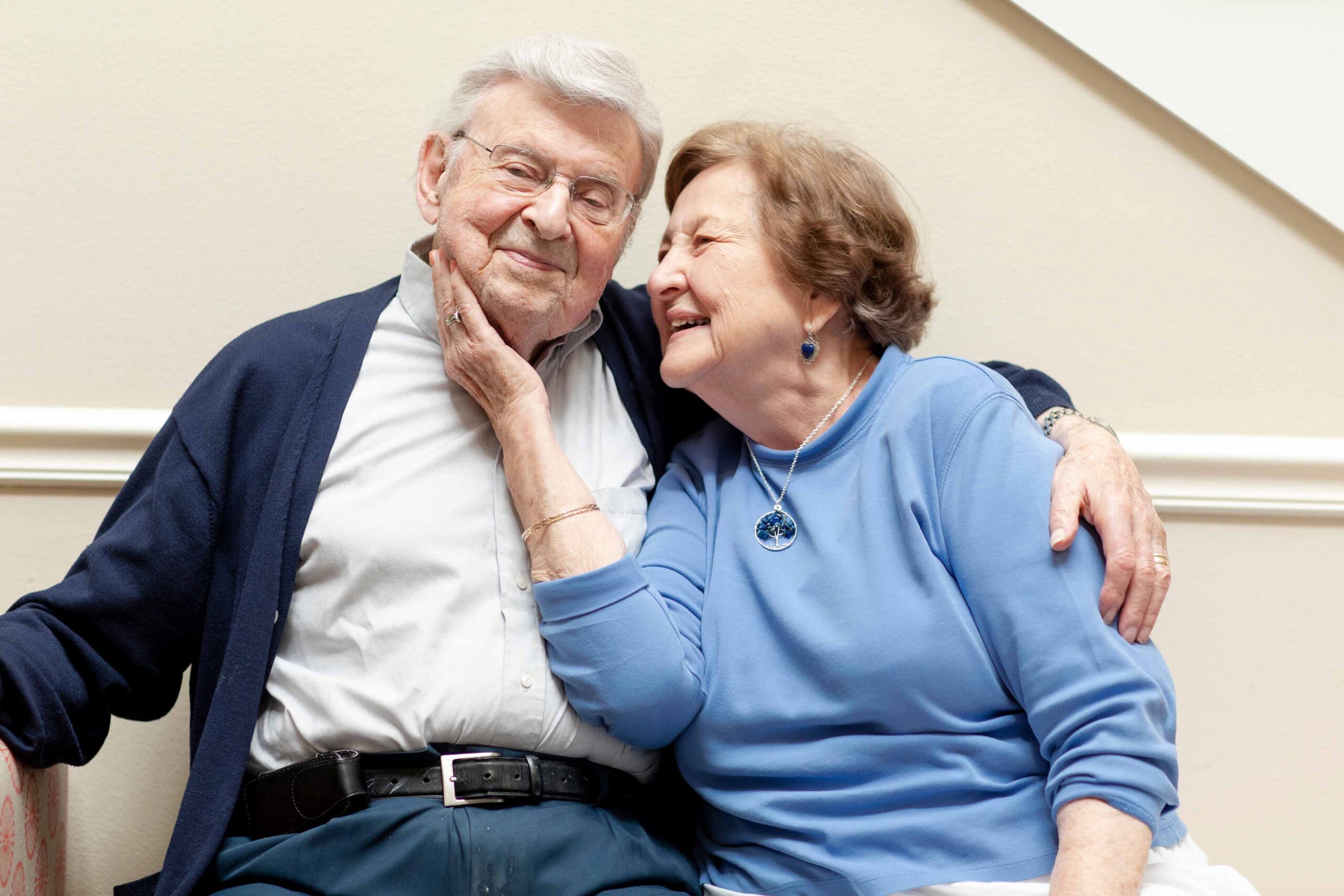 Grace_Management_Memphis_2018-2281 - The Residence at Whitehall An older white man is sitting down and smiling as he's hugging an older white woman, who's holding his face and smiling.