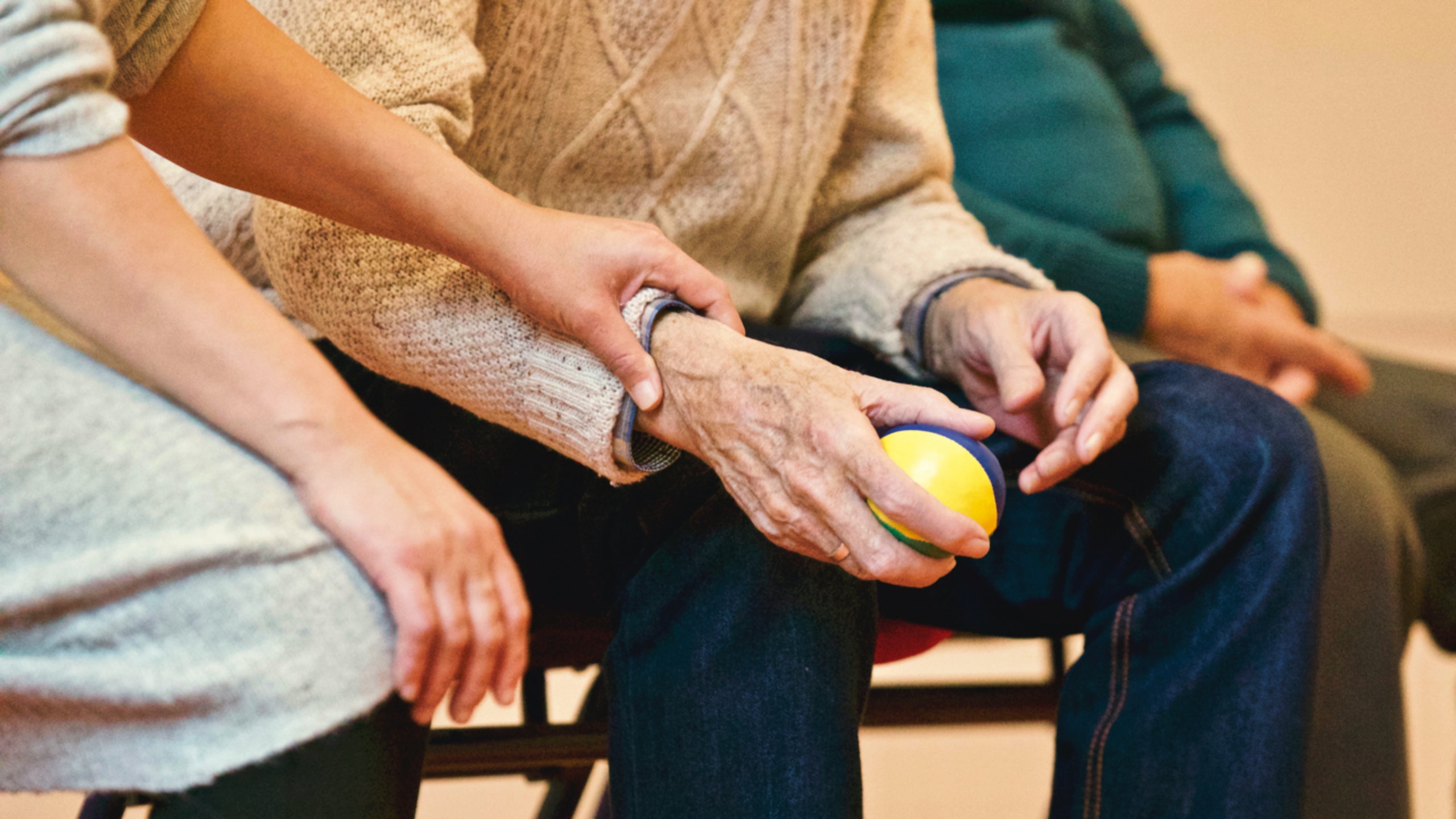 pexels-matthias-zomer-339620 - The Residence at Whitehall An up-close shot of an older person's hands holding a colorful stress ball, and a pair of younger hands holding the older person's ones.