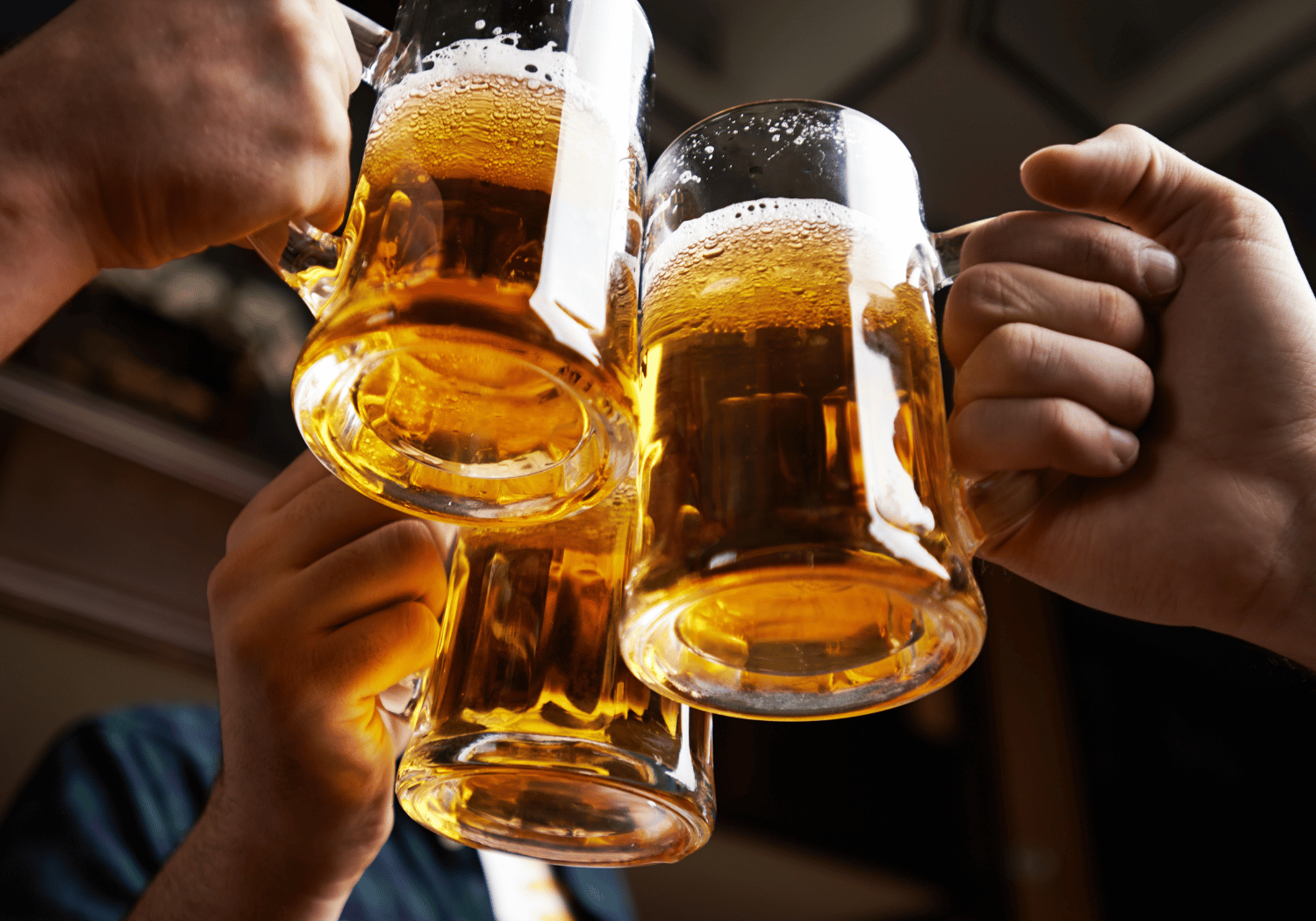 People raising and clinking frosty beer mugs in a cheers toast, golden beer and foam visible.
